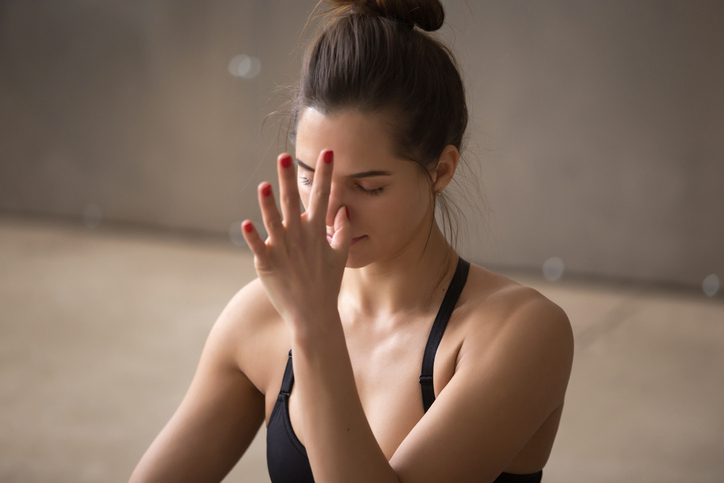 Young attractive woman making nadi shodhana pranayama, grey stud